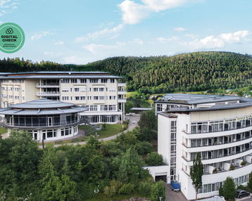 Moderne Gebäude in einer grünen Umgebung, umgeben von Bäumen und Hügeln. Ein Gebäude hat eine runde Form mit großen Fenstern.